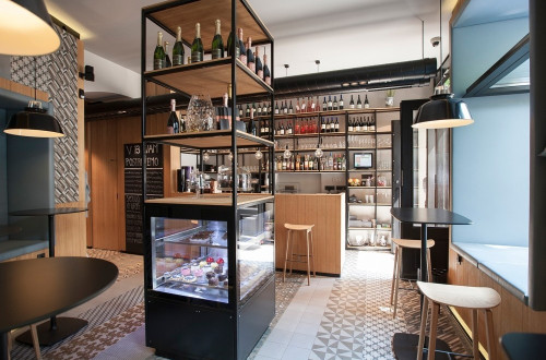 The interior of a café. A display of wine bottles and pastries.